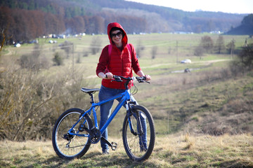 Beautiful young woman bathes in the rays of the spring sun on a hill above the river. Beautiful young woman with bicycle.