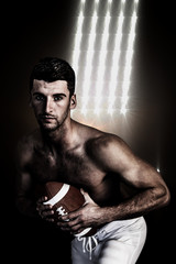 Fototapeta na wymiar Portrait of shirtless rugby player posing with the ball against spotlights