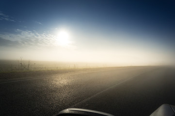 The dim sun shines through the thick morning fog on the highway