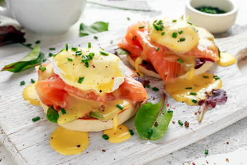 Eggs Benedict on english muffin with smoked salmon, lettuce salad mix and hollandaise sauce on white board - obrazy, fototapety, plakaty