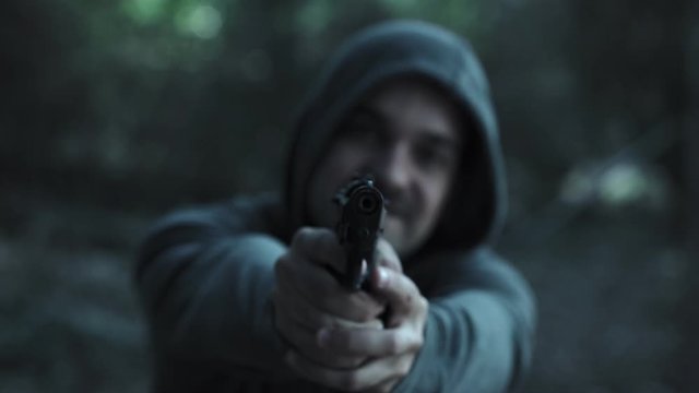 Crazy hooded young man pointing the gun at the camera