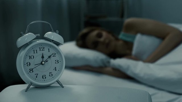 Woman sleeping in bed with alarm clock showing midnight time, night dreams 