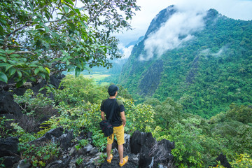 Asian young man traveler with his camera backpack stands on rocky cliffs. Relax in a holiday.