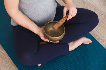 Pregnant woman doing prenatal yoga meditating with Tibetan singing bowl