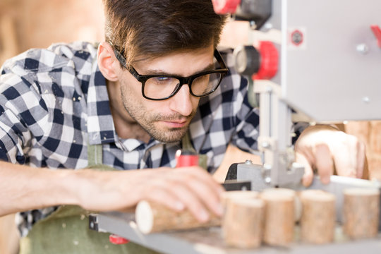 Portrait Of Handsome Artisan Cutting Piece Of Wood  Using Machine Unit With Sawdust And Woodchips Flying Off While Working In Modern Carpenters Shop, Copy Space