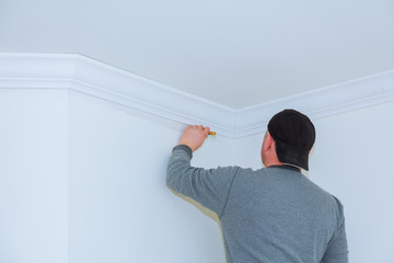 Installation of ceiling moldings. Worker fixes the wood molding to the ceiling