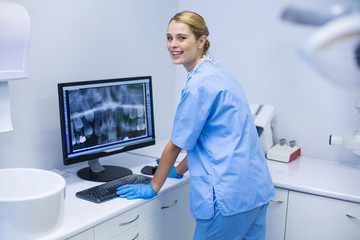 Portrait of female nurse examining x-ray report on computer - obrazy, fototapety, plakaty