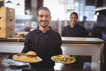 Portrait of smiling young waiter serving food while standing against waitress