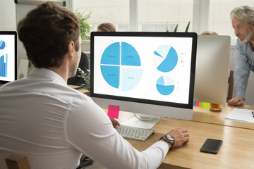 Young man employee using computer application with charts on screen preparing annual report in...
