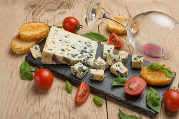 Cheese dor blu with cherry tomatoes and basil, with a glass of red wine, on a wooden texture