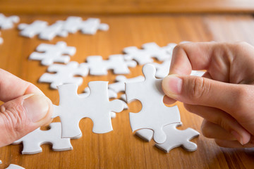Close up of hand connecting jigsaw puzzle with wooden background, business solutions, success and strategy concept