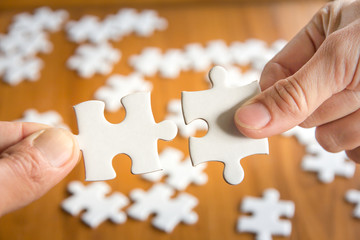 Close up of hand connecting jigsaw puzzle with wooden background, business solutions, success and strategy concept