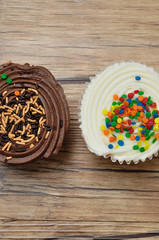 A chocolate and a white cupcake displayed on a wooden background