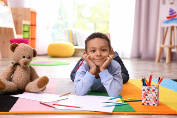 Little African-American boy drawing on floor indoors