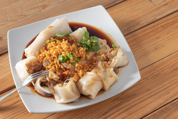 close up of tube noodles on plate, with deep fried garlic,soy sauce and coriander on top on wood background
