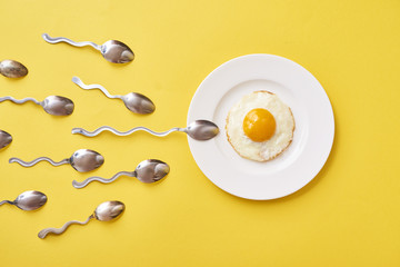 Conception of fertilization. Fried egg in white plate, and spoon - obrazy, fototapety, plakaty