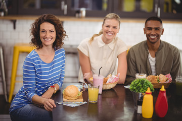 Portrait of smiling friends sitting with food and drink at coffee shop