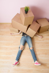 Photo of woman in jeans lying under cardboard boxes