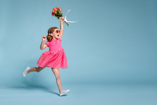 funny child girl runs and jumps with bouquet of flowers on colored background