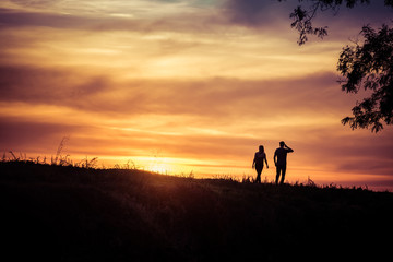 A couple of man and woman is walking and looking at amazing and beautiful sunset, with tree on one...