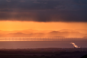 Fototapeta na wymiar Windmills at sea during sunset golden hour