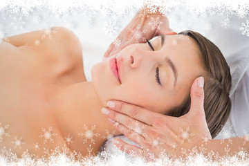 Attractive young woman receiving facial massage at spa center against fir tree forest and snowflakes