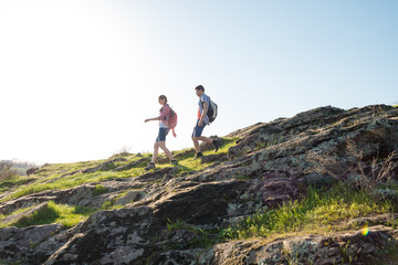 Young Happy Couple Hiking with Backpacks on the Beautiful Rocky Trail at Sunny Evening. Family Travel and Adventure.