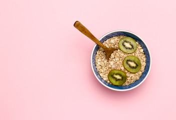 A bowl of oatmeal with kiwi on a pink background.