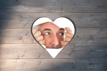 Man looking through torn paper against heart in wood