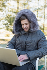 Young man in warm clothing using laptop in the forest