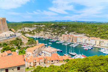 Fototapeta na wymiar BONIFACIO PORT, CORSICA ISLAND - JUN 24, 2015: View of beautiful port with colorful houses and boats on sunny summer day. This French island is popular tourist destination in Europe.