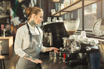 Tattooed barista making coffee in professional coffee machine - obrazy, fototapety, plakaty