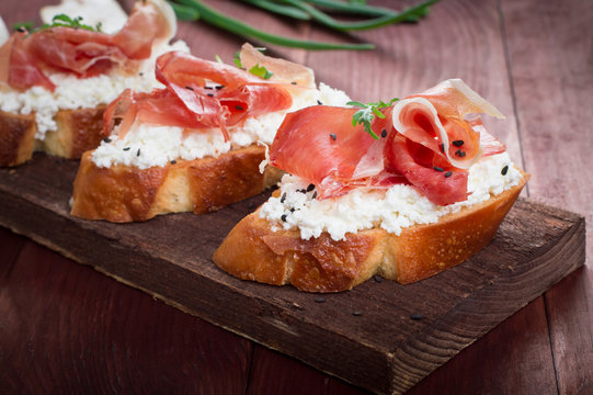 Baguette with cottage cheese, arugula and ham, sandwich on a board, selective focus. Wooden rustic background. Top view