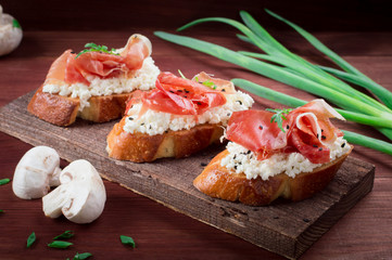 Baguette with cottage cheese, arugula and ham, sandwich on a board, selective focus. Wooden rustic background. Top view