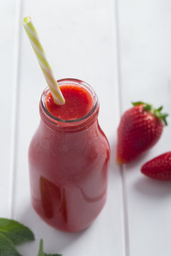 Fresh strawberry smoothie in bottle on a white wooden rustic background