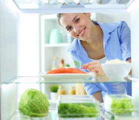 Portrait of female standing near open fridge full of healthy food, vegetables and fruits