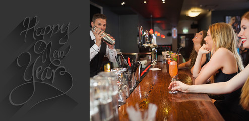 Handsome bartender making cocktails for beautiful women against classy new year greeting