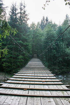 Fototapeta Suspended wooden bridge across the mountain river.
