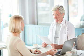 Confident economist with papers listening to strategy of his colleague during start-up meeting in...