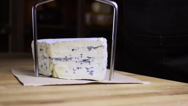 Blue cheese is cut with a cheese knife. Cheese shop. Cheese with blue mold. Slow motion.