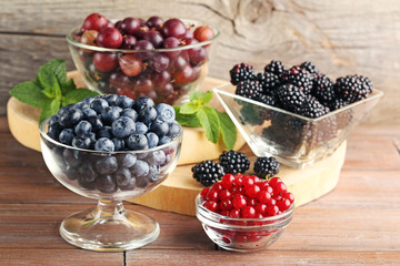 Ripe and sweet berries in glass bowls on wooden table