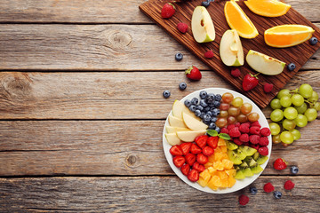 Fresh fruits in plate with cutting board on grey wooden table