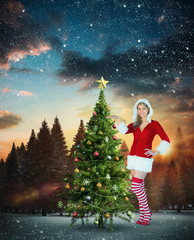 Pretty girl presenting in santa outfit against fir tree forest in snowy landscape