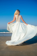 Fototapeta na wymiar beautiful and happy bride in a chic long white wedding dress whirls and dances on the beach. wedding dress evolves and flies during a dance on the beach