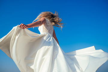 beautiful and happy bride in a chic long white wedding dress whirls and dances on the beach....