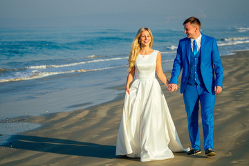 Fototapeta na wymiar handsome groom in a chic suit and a beautiful bride in a wedding gown walk along the beach. concept of a chic and rich wedding ceremony on the beach