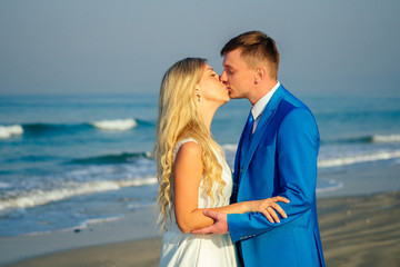 handsome groom in a chic suit and a beautiful bride in a wedding dress hug and love each other on the beach. concept of a chic and rich wedding ceremony on the beach