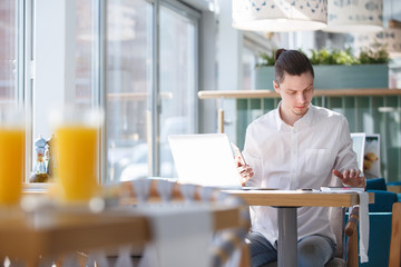 Cute young financial analyst works remotely on a laptop and smartphone using high-speed Internet in a cafe