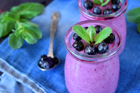 Blueberry smoothie in glass jars topped with berries and mint on blue background