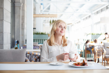 Obraz na płótnie Canvas Satisfied young woman enjoys a cup of coffee sitting in a light stylish cafe before work in the morning